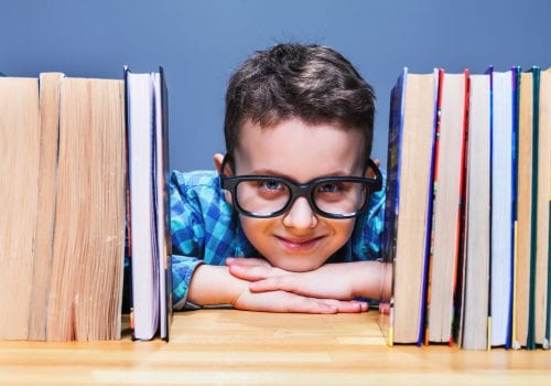 Happy pupil in glasses against books