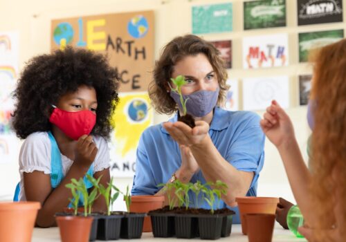 Female teacher wearing face mask showing plant pots to students in class